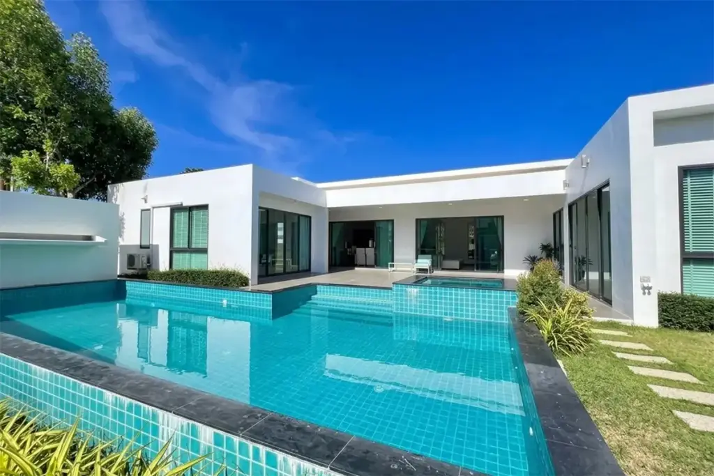 Palm Lakeside Villas rectangular swimming pool with lounge chairs, green lawn, and modern house with sliding glass doors.