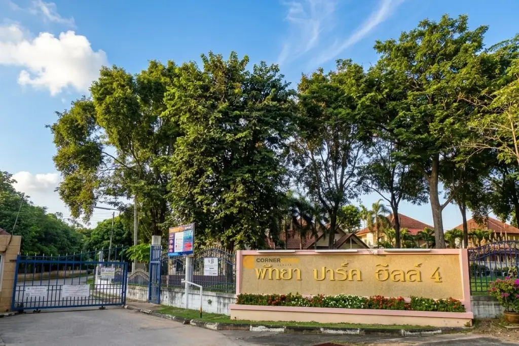Pattaya Park Hill 4 entrance sign in Thai script, with green letters on a beige wall and trees in the background.
