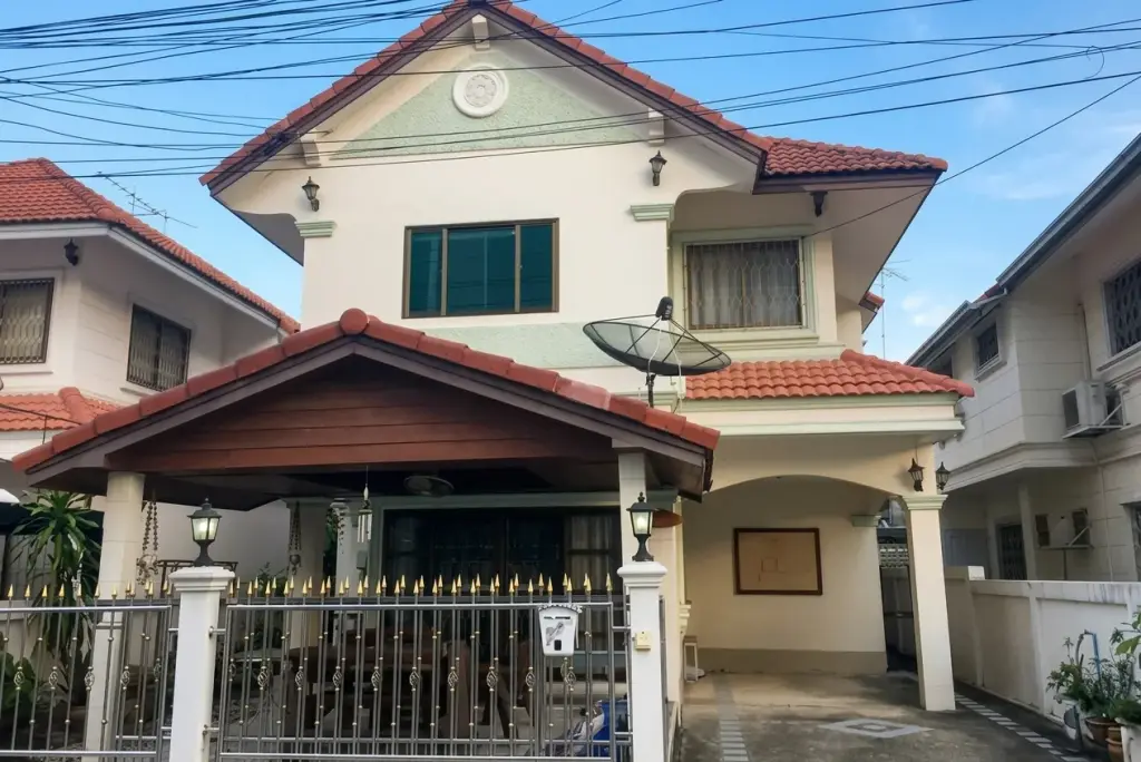 Tueanjai Village, front exterior of a two-story house with red tiled roofs, a covered carport, and a metal gate.