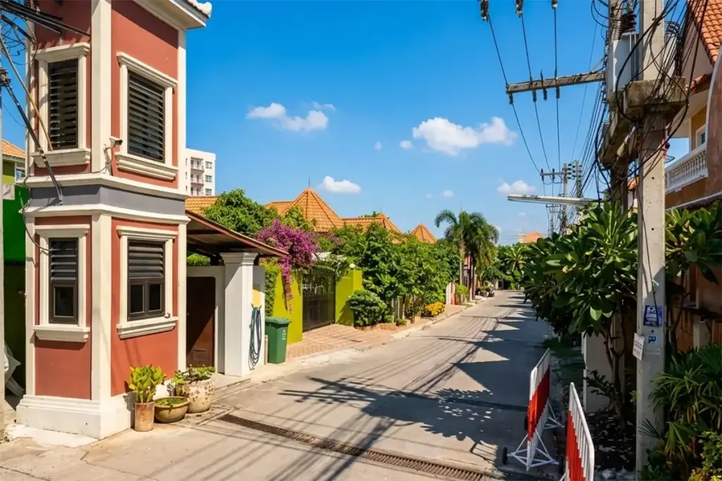 Thanyawan Home: Light green two-story house with brown roof, striped awning, and lush green garden foliage in front.