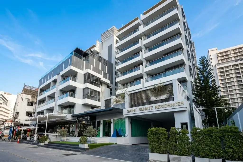 The Senate Residences, a modern white and grey building exterior with glass balconies and ground-floor shops.