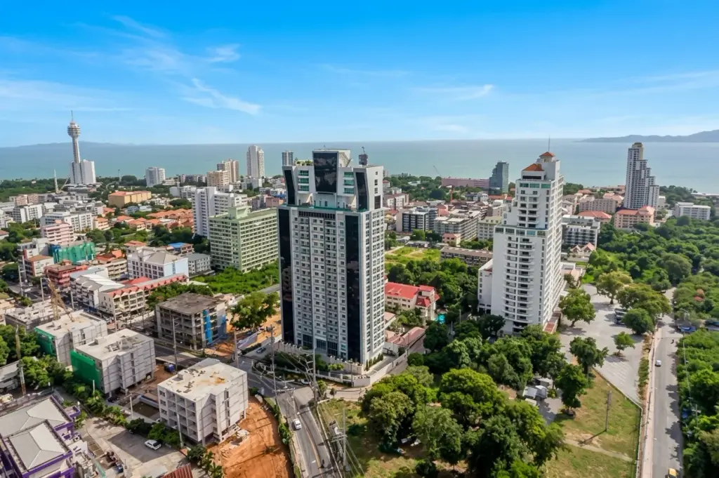 The Vision: Aerial view of Pattaya cityscape with high-rise buildings, ocean, and distant mountains under a blue sky.