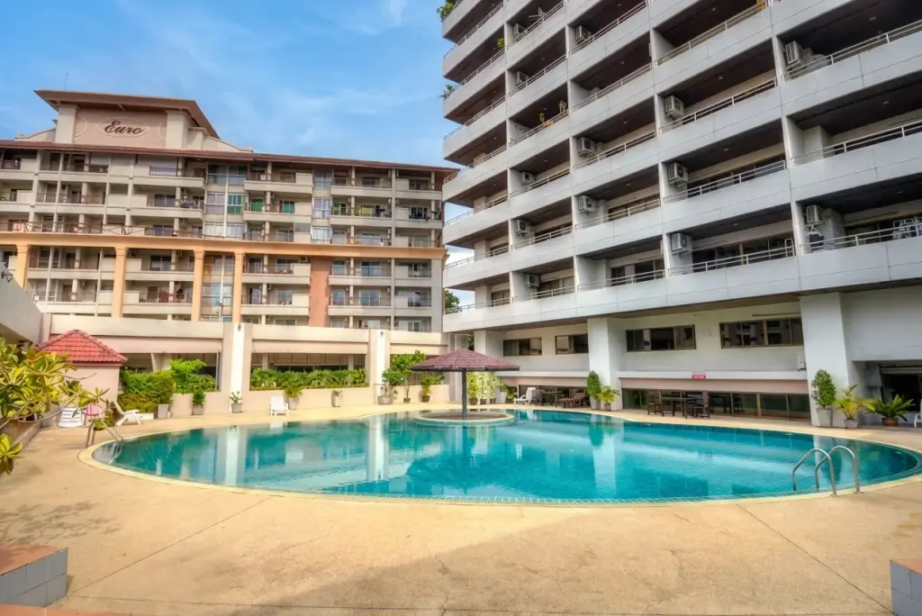 PKCP Tower outdoor swimming pool with surrounding buildings, lounge chairs, and a central umbrella.