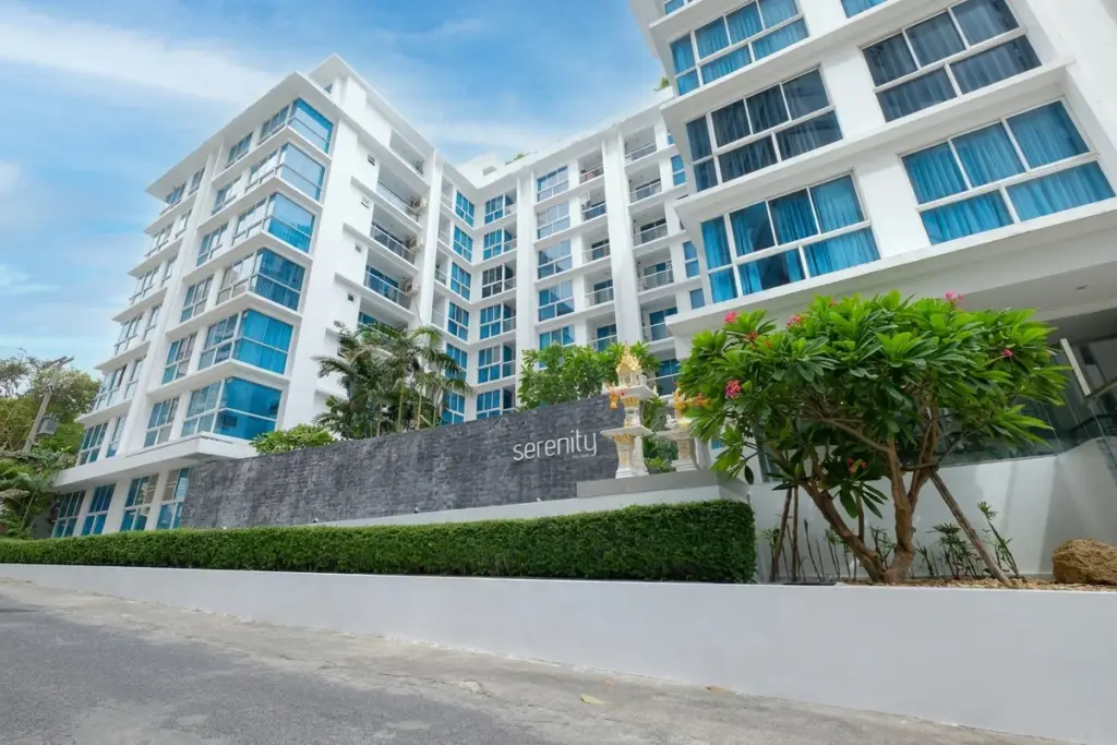 Serenity Wongamat condo building exterior with modern white facade, blue windows, and lush green landscaping.