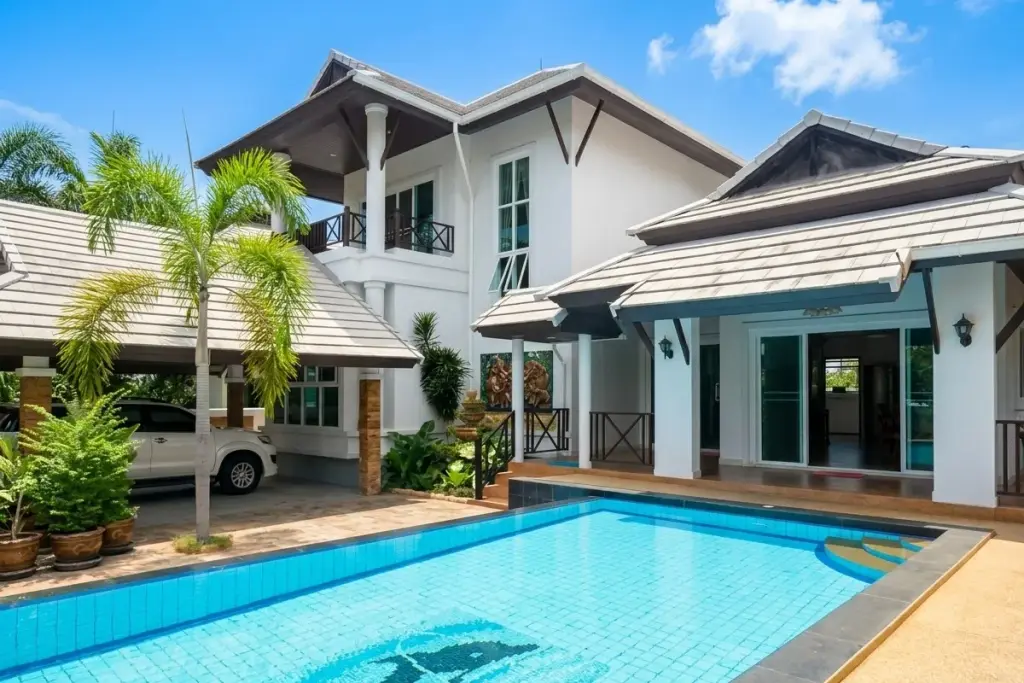 Baan Samran: Exterior view of the property with a swimming pool featuring a dolphin mosaic, covered carport, and lush greenery.