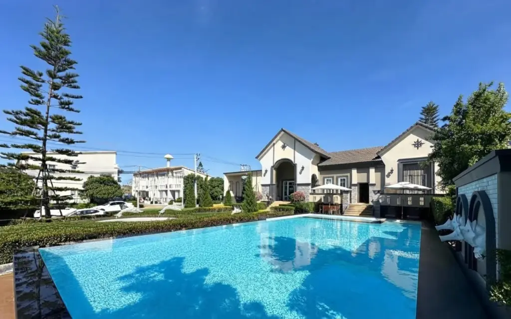 Golden Town Pattaya large blue swimming pool with a house featuring a gabled roof and outdoor seating areas in the background.