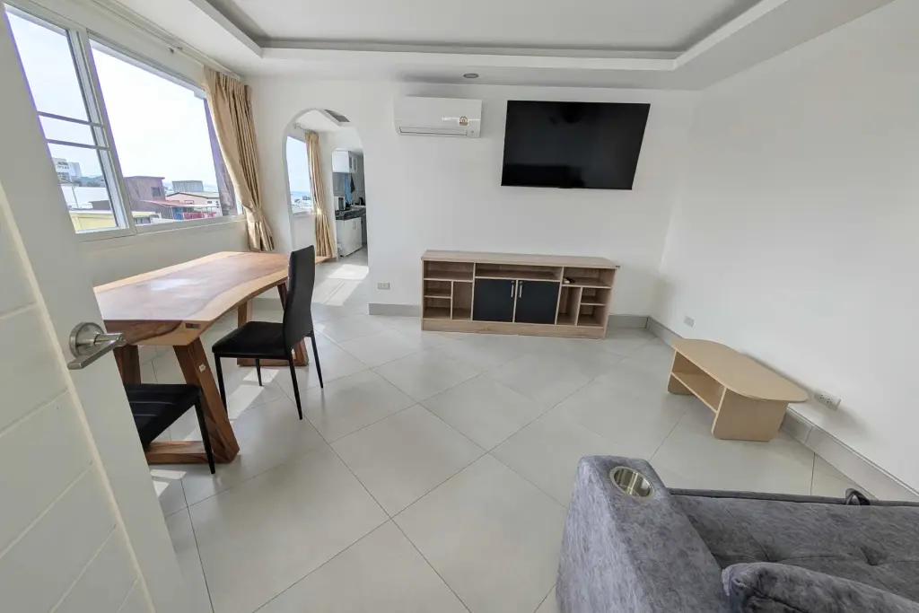 1 Bedroom Condo for Rent at Pattaya Beach Condo living room with wooden dining table, TV unit, and city view windows