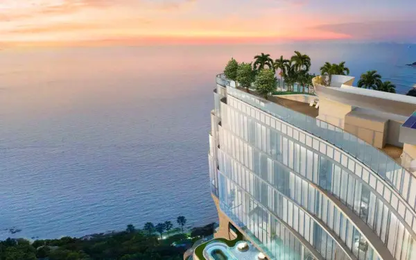 Wyndham Grand Residences Wongamat modern high-rise building with curved glass balconies and rooftop garden overlooking the ocean at sunset.