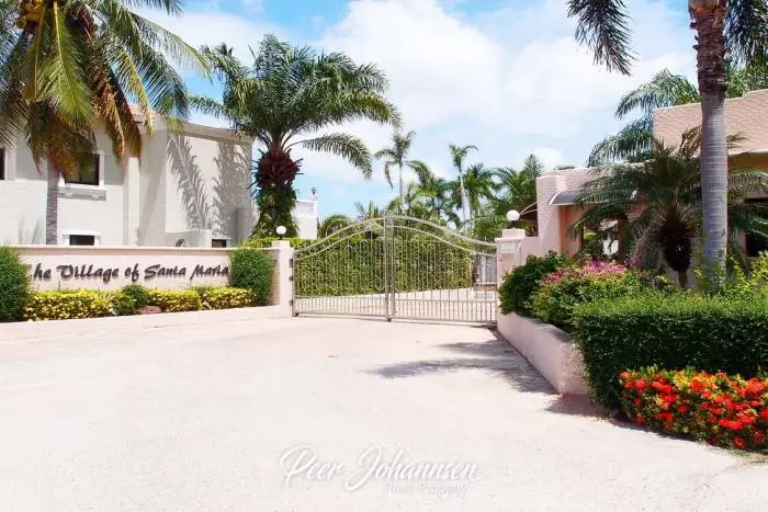 Santa Maria entrance gate with lush tropical landscaping, palm trees, and the community sign for The Village of Santa Maria.