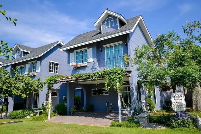 Winston Village light blue house with covered patio, climbing vines, dormer windows, and green lawn.