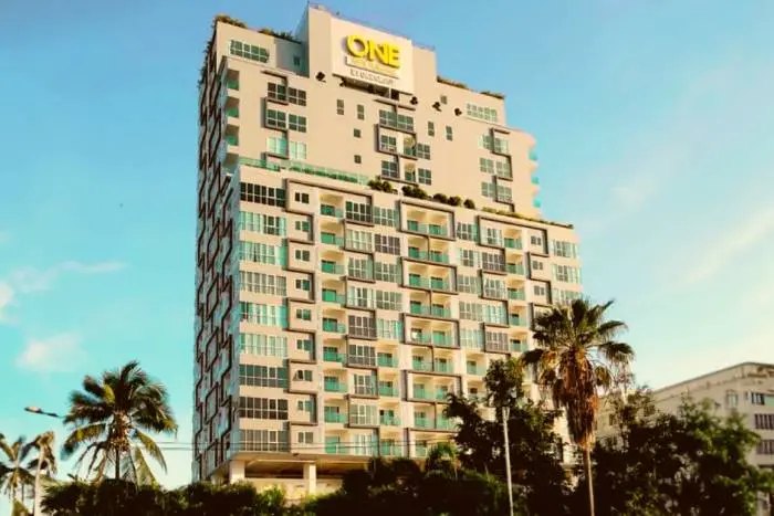 One Tower Pratumnak exterior of the tall modern condo building with balconies and palm trees against a blue sky.