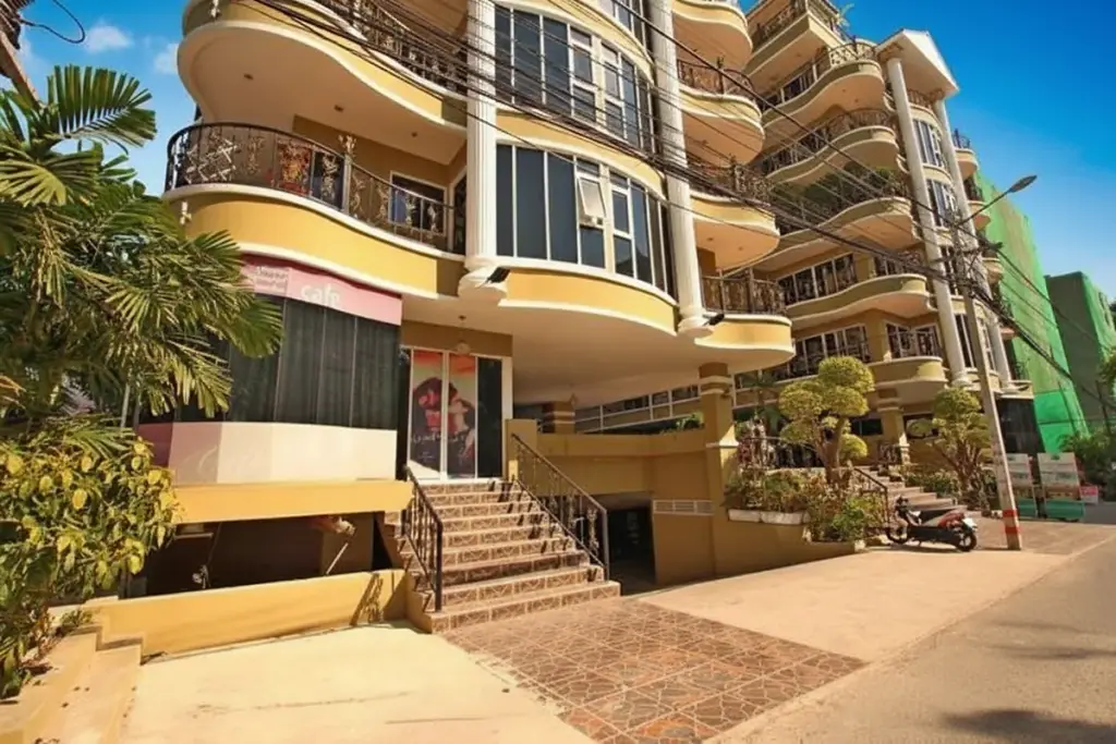 Siam Oriental Twins building exterior with main entrance stairs, cafe, and palm trees on a sunny day.