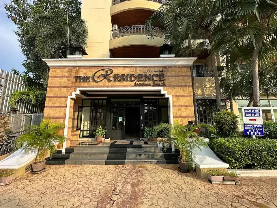 The Residence Jomtien condo entrance with stone facade, palm trees, and signage