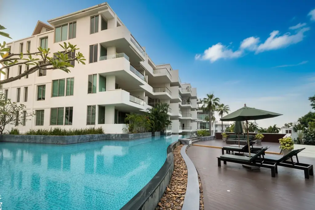 The Sanctuary Wongamat. Modern white condo building with balconies, a curved swimming pool, and sun loungers on a wooden deck.