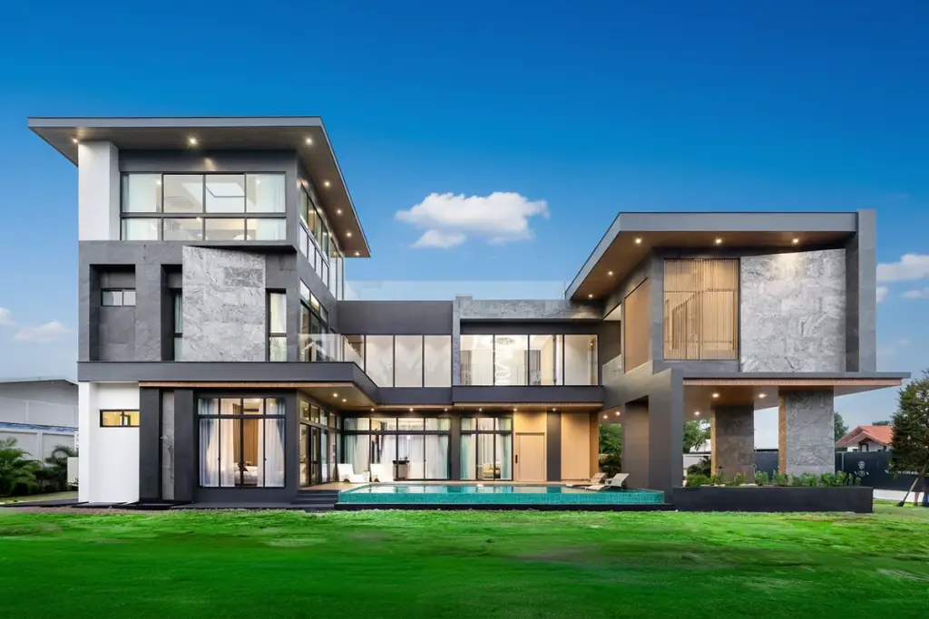 The Sylva Pattaya modern house exterior with pool, large glass windows, and green lawn at dusk.