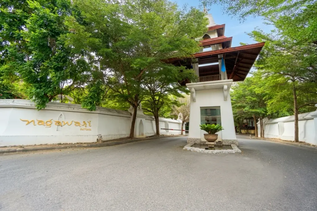 Nagawari Pattaya main entrance gate with white wall, gold lettering, traditional Thai-style security booth, and lush green trees.