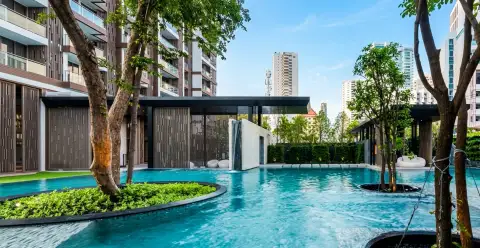 Baan Plai Haad large outdoor swimming pool with trees, modern building entrance, and city skyline.