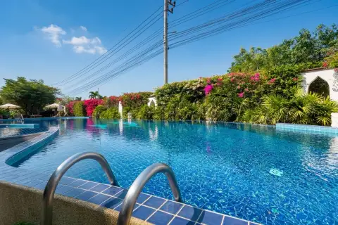 Sunrise Beach Residence large outdoor swimming pool with blue mosaic tiles, surrounded by lush greenery and flowering bushes.