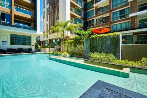 The Urban Pattaya sunlit pool area with loungers, orange umbrella, and tropical greenery