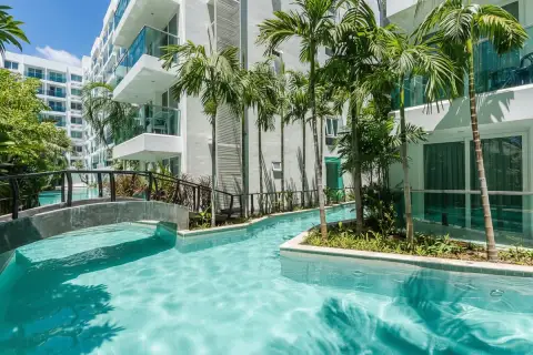 Amazon Residence winding swimming pool with palm trees, tropical plants, and a small bridge.