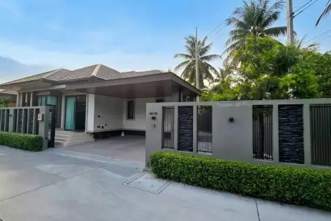 Amarin House 2 front facade with covered carport, decorative gate, manicured hedges, and tropical palm trees