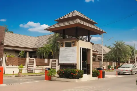 Baan Piam Mongkhon security gatehouse with a traditional roof and a car passing through the barrier.
