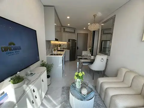 1 Bedroom Condo for Sale at Copacabana Coral Reef living room with wall-mounted TV showing development branding