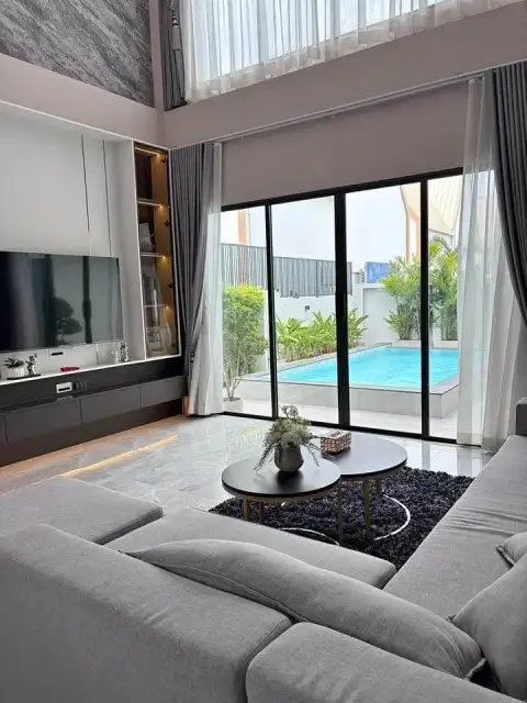 4 Bedroom House for Sale in East Pattaya double-height living room with gray sofa and pool view through glass doors