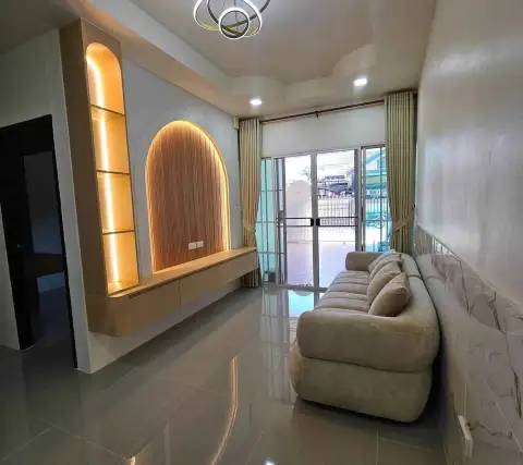 2 Bedroom Townhouse for Sale in East Pattaya living room with beige sofa, arched wooden TV feature wall, and glass doors to patio