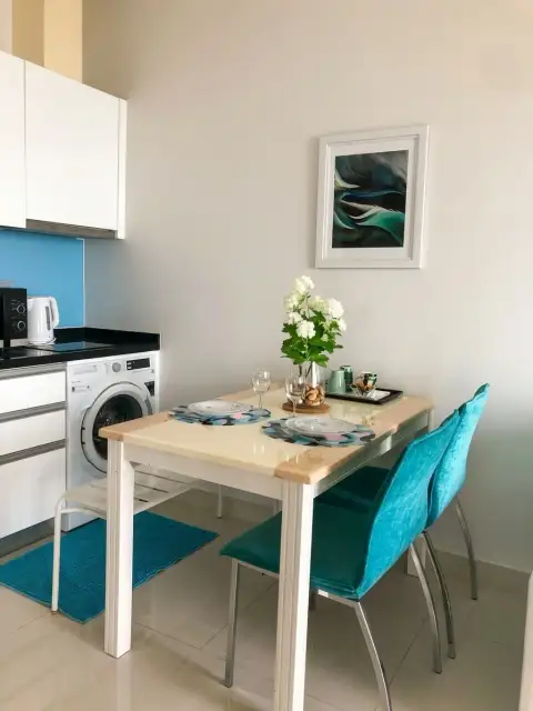 Studio Condo for Sale at Musselana dining table with teal chairs beside compact kitchen and washer