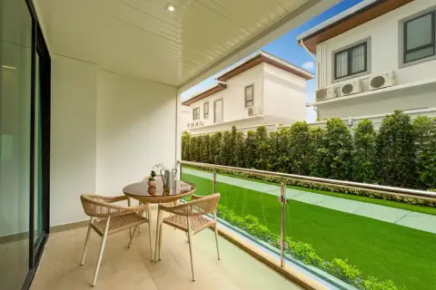 Gardenia Pattaya balcony with a small round table, two chairs, and a view of the green lawn and neighboring houses.