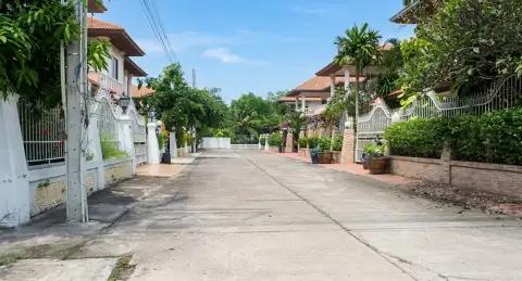 Eakmongkol Village Chaiyapruek 2 lush green garden area with potted plants, grass, and a brick wall.