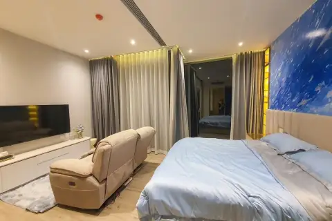 1 Bedroom Condo for Sale & Rent at Arom Wongamat wide-angle bedroom view with king bed, recliner sofa, TV unit, and blue feature wall