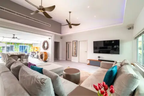 5 Bedroom House for Sale & Rent in Huai Yai open-plan living room with sectional sofa, wall-mounted TV, and pool view