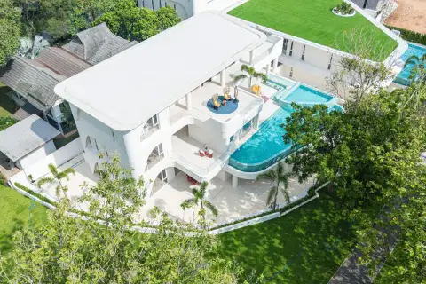 6 Bedroom House for Sale in Huai Yai bird's eye drone view of white villa with curved infinity pool and green landscaping