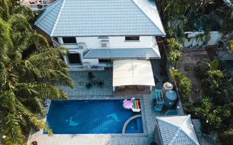7 Bedroom House for Rent in Jomtien aerial view of swimming pool, patio, and tiled roof house surrounded by palms