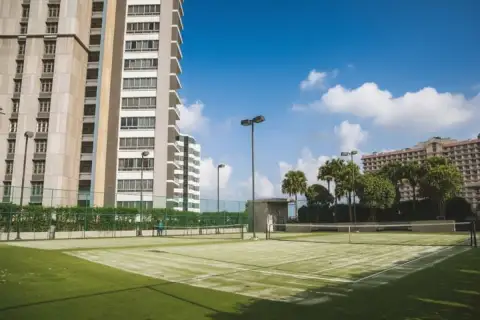 Northpoint outdoor tennis court with green surface, surrounded by palm trees and tall condo buildings.
