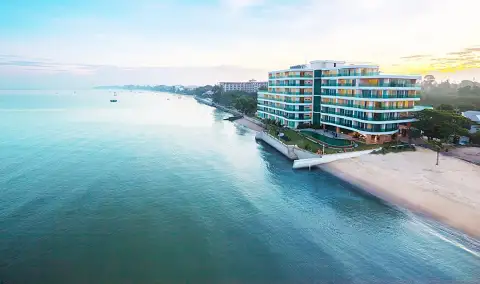 Paradise Ocean View: Aerial view of the pool, green lawn, sandy beach, and ocean with city skyline in distance.