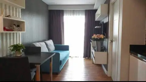 1 Bedroom Condo for Sale in Jomtien living room with teal sofa, dining table and floral centerpiece near window