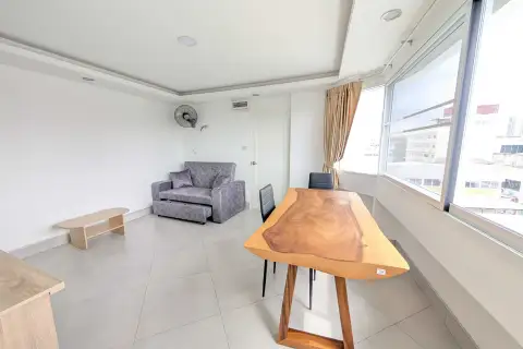 1 Bedroom Condo for Rent at Pattaya Beach Condo lounge area with gray sofa, dining table, and bright city-view windows