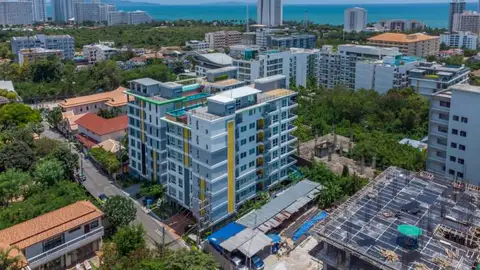 Estanan Condo: Aerial view of the condo building in Pattaya, surrounded by other buildings and green spaces, with the ocean in the background.