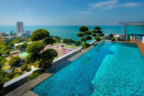 One Tower Pratumnak rooftop infinity pool overlooking the city skyline and ocean under a clear blue sky.
