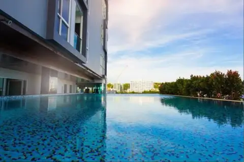 One Tower Pratumnak ground level swimming pool reflecting the building and blue sky, with surrounding trees.
