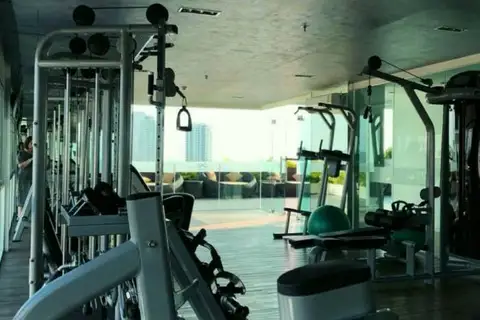 One Tower Pratumnak interior view of the modern gym with exercise equipment and an outdoor terrace visible through glass.