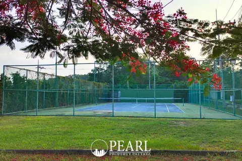 Nibbana Shade outdoor tennis court enclosed by a fence, surrounded by green grass and trees.