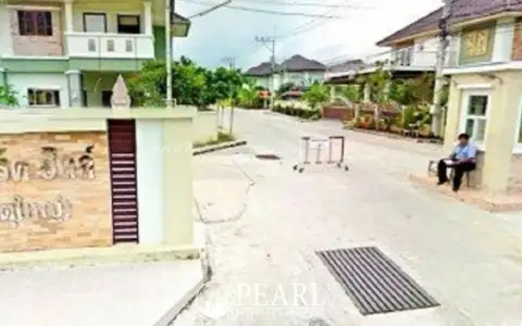Park Hill Village entrance with a security guard sitting, a sign with Thai text, and houses in the background.