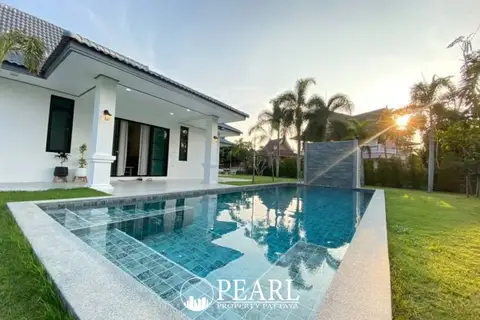 The Lanterns outdoor swimming pool with a water feature, green lawn, and a modern house at sunset.