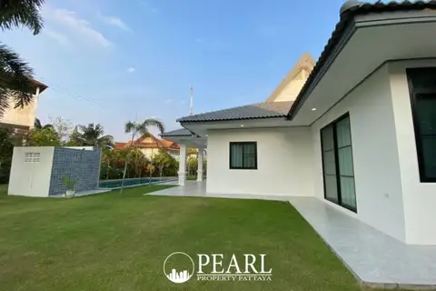 The Lanterns outdoor swimming pool with a water feature, green lawn, and a modern house at sunset.