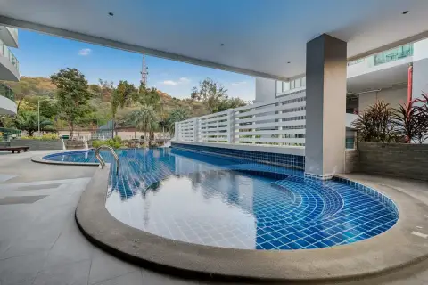 The Lofts Pratumnak covered swimming pool area with blue tiles, lush green hills, and distant buildings.