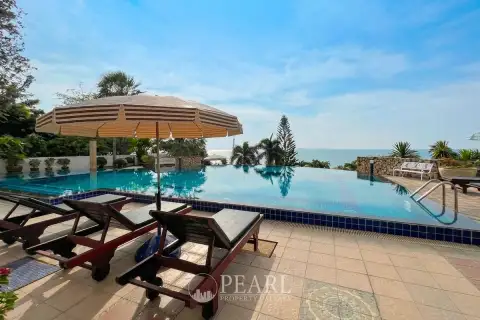 Baan Rimpha swimming pool area with blue and white striped umbrella, wooden sun loungers, and lush greenery.